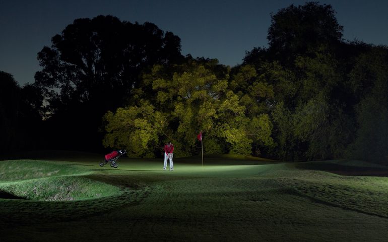 Lone male golfer putting green at night