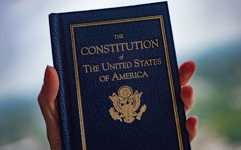 The Constitution of The United States of America book in hand on blurred background.