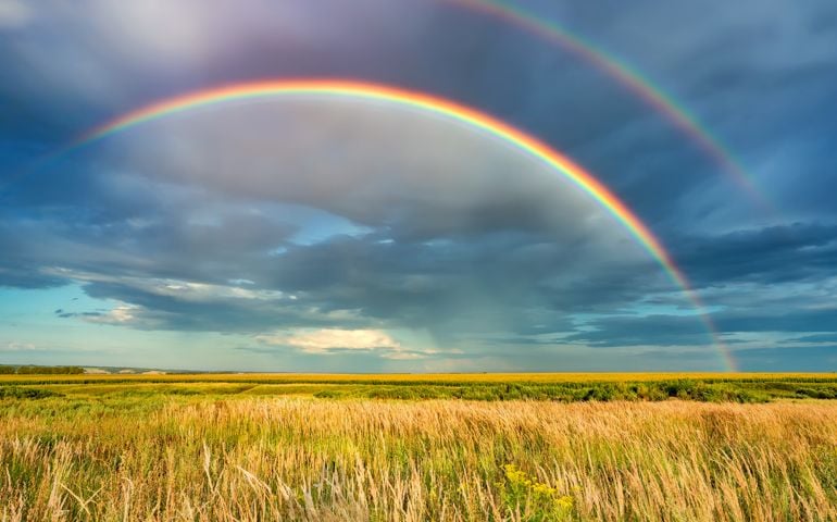 Rainbow over stormy sky. Rural landscape with rainbow over dark stormy sky in a countryside at summer day.