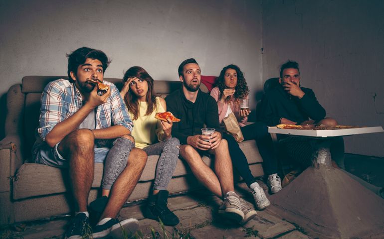 Group of young friends watching a horror movie on a building rooftop terrace, eating pizza, drinking beer and having fun