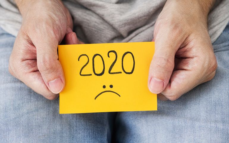 Man holding yellow piece of paper with the year 2020 and a sad smiley on it in his hands. 2020 horrible year concept. Close up.