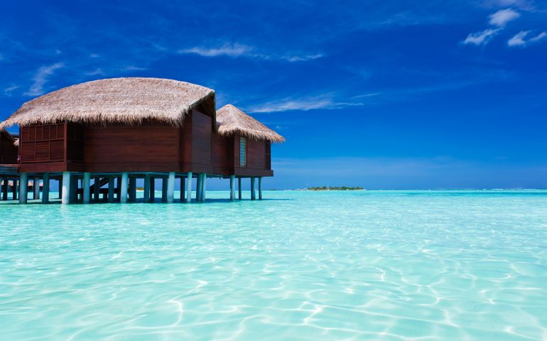 Overwater bungalow in blue lagoon around tropical island