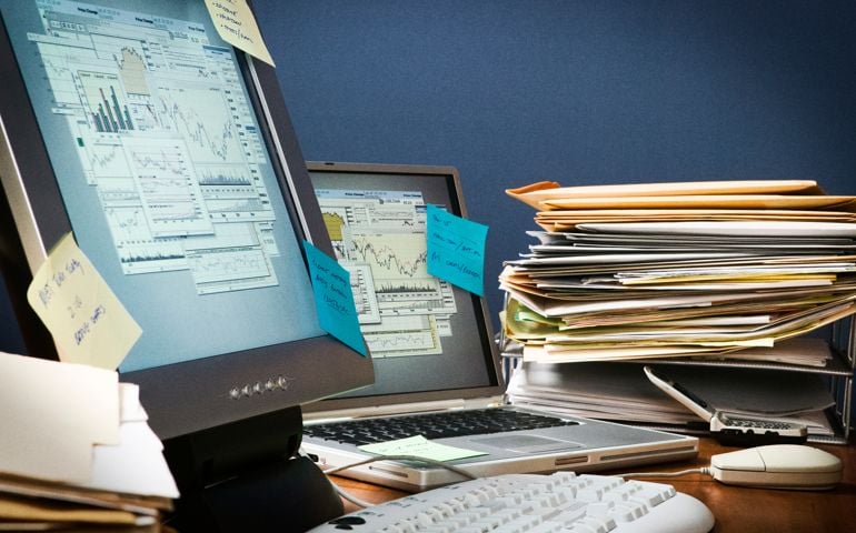 Office desk cluttered with paperwork, post-it-notes and files.