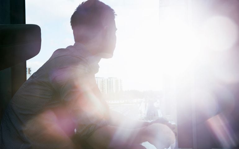 silhouette of man looking out window with flare