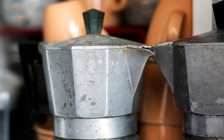 Close-up view of an old rusty coffee pot inside a pantry. Scratches and signs of wear near the spout.