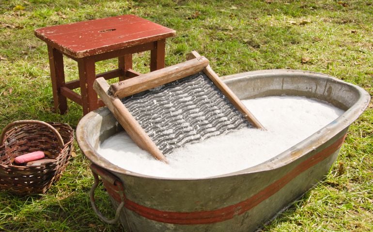 An old fashioned washing trougth filled with water, a vintage washboard and soap that wash the laundry