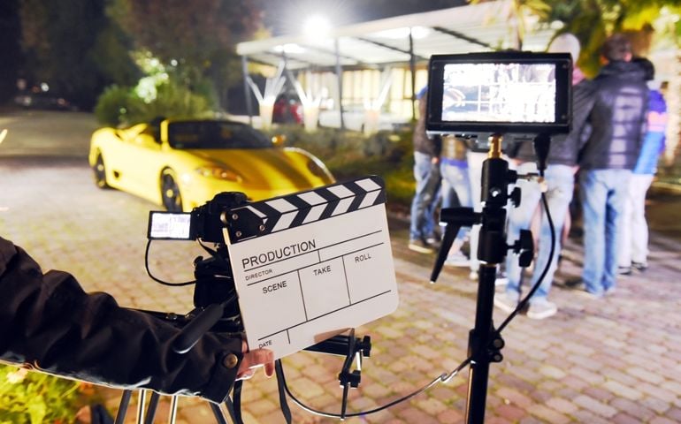 Operator holding clapperboard during the production of short film outdoor in the night with sportive yellow car and actor on stage