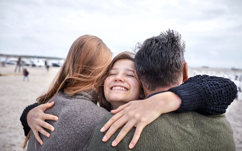 Happy girl hugging woman and man on the beach
