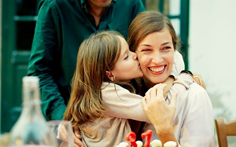 Cute girl kissing mother on cheek while celebrating birthday at outdoor table in yard
