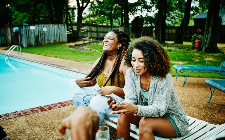 Laughing woman hanging out with friends by backyard pool on summer evening