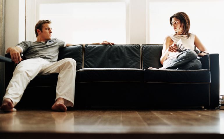 Young couple sitting on either end of sofa, looking at each other