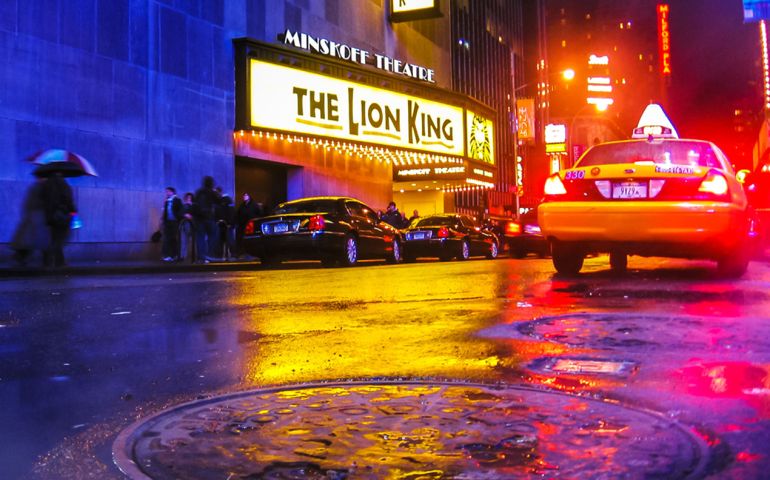 The Lion King, Times Square theater for Broadway shows, city street by night with local taxi and a smoking manhole
