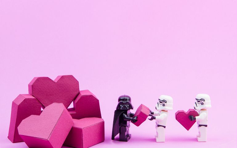 Lego stormtrooper give paper box red heart shape to lego darth vader on pink background