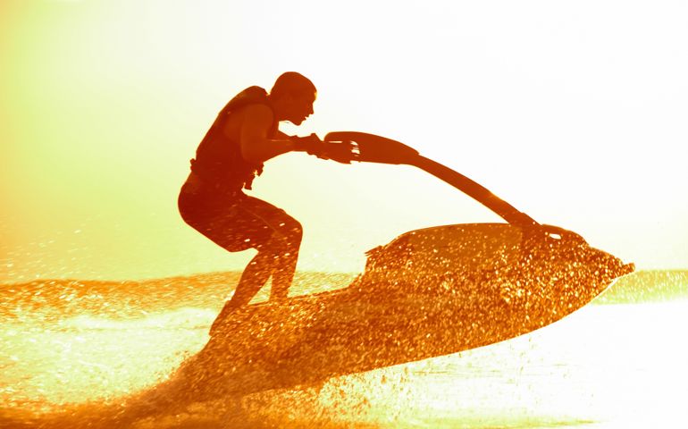 strong man jumps on the jetski above the water at sunset