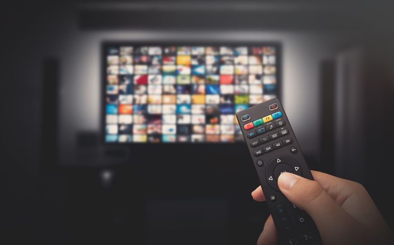 Multimedia video concept on TV set in dark room. Man watching TV with remote control in hand.