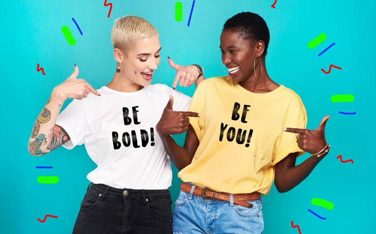 Studio shot of two confident young women pointing at their statement t shirts against a turquoise background