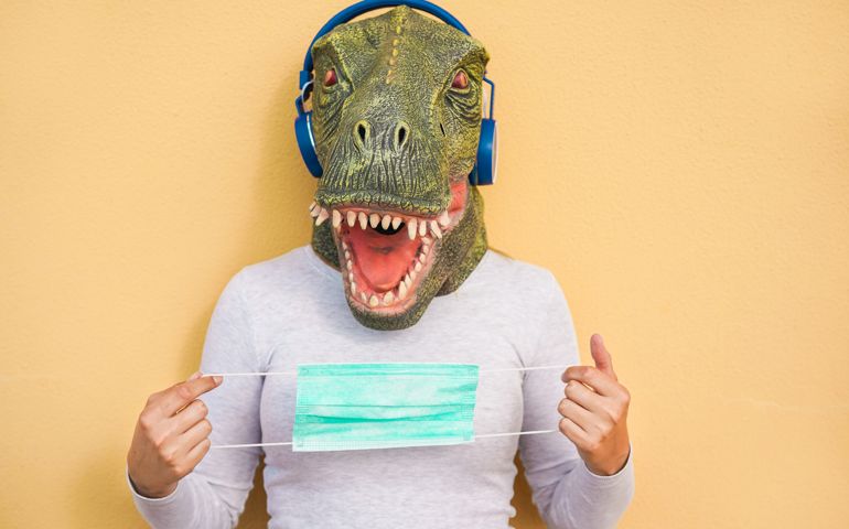 Crazy woman wearing t-rex and medical protection masks while listening music with headphones - Quarantine isolation lifestyle during coronavirus time - Absurd and funny trend concept - Focus on face