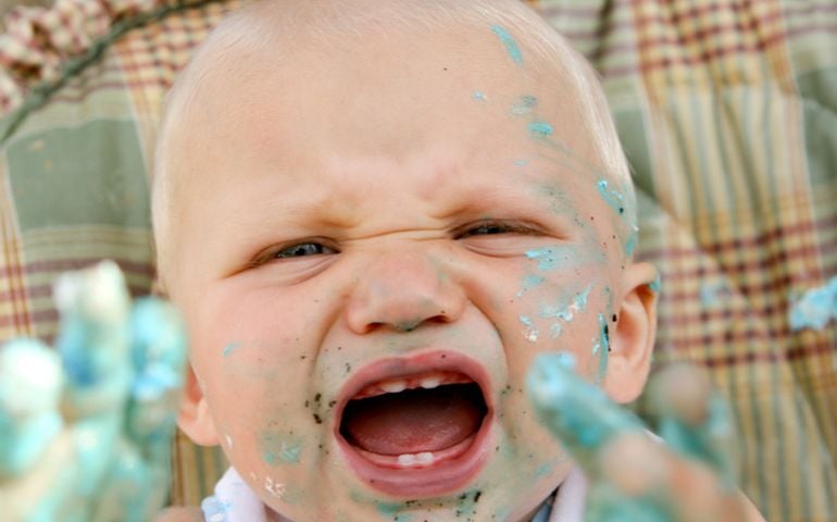 A 1 year old shows off his new teeth while reaching for you with frosting covered hands!