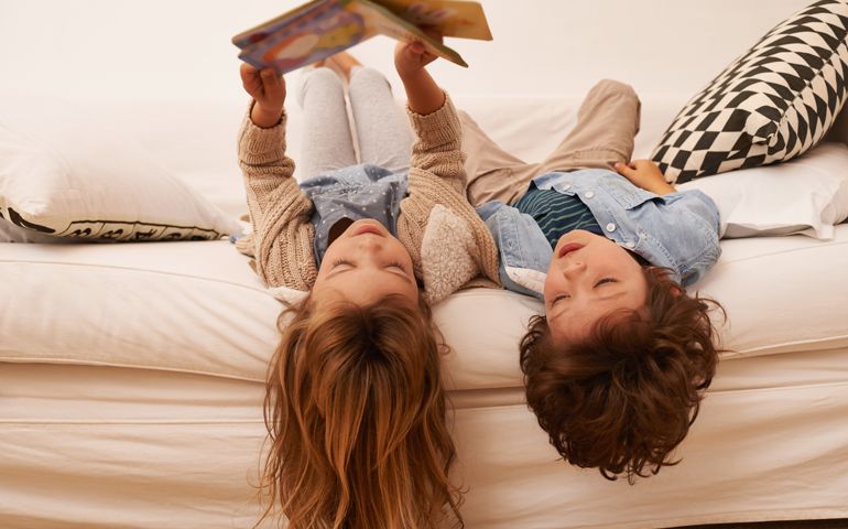 Shot of two young children lying on their backs and reading a book together