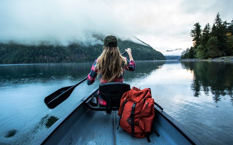 A woman paddling a canoe across a lake early in the morning.