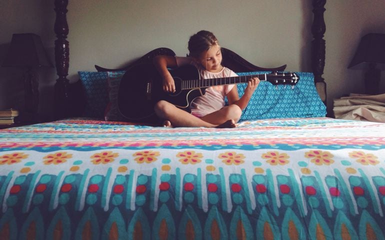 Young girl sitting on a bed playing the guitar