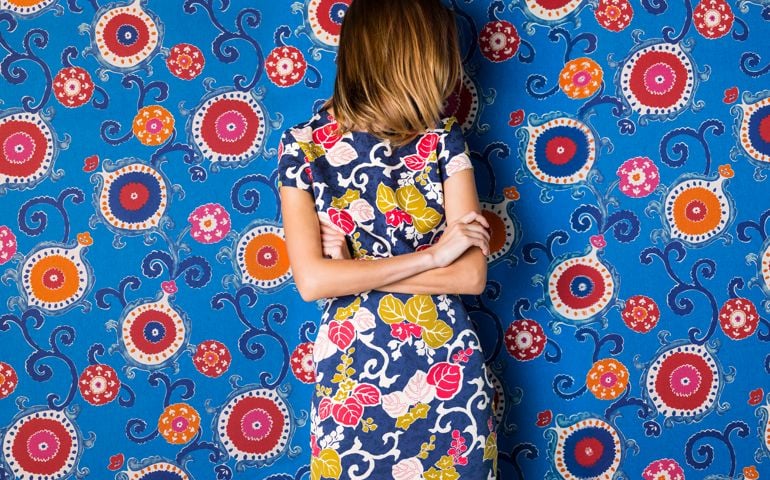 Beautiful young woman wearing blue floral, leaf print dress against blue, red, and orange floral print background with her hair hiding her face