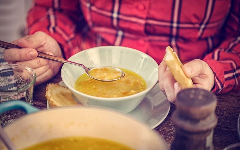 Little girl eating delicious chicken soup with carrots, onions and parsnips. The soup is served in a bowl with creme fresh and grilled toast.