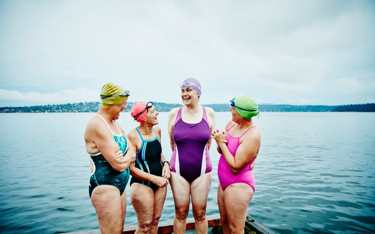 Laughing mature female swimmers standing on dock preparing for early morning swim