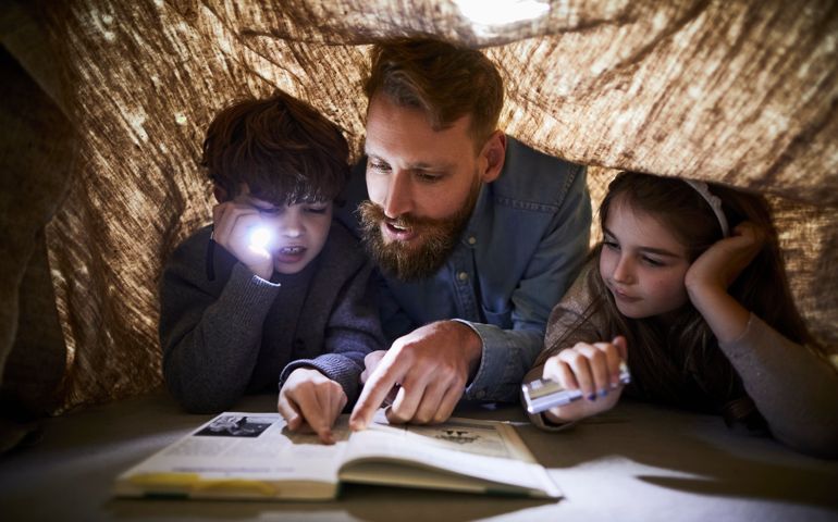 Father reading book to children under a cloth