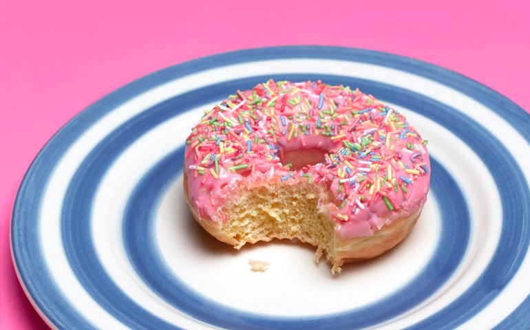 Close up of a pink iced doughnut on blue stripped plate on pink background.