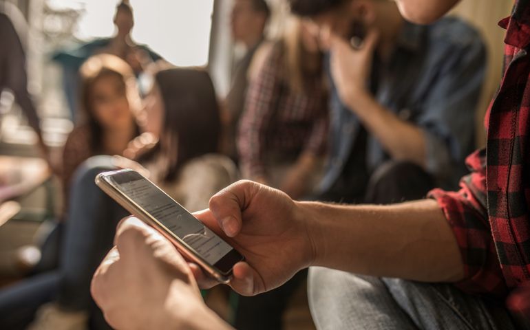 Unrecognizable male student text messaging on mobile phone while being on a break in the classroom.