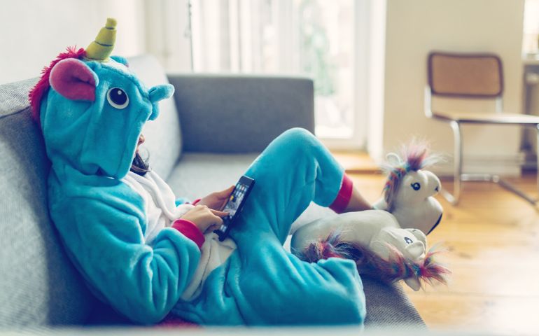 little girl in unicorn costume relaxing with mobile on couch at home