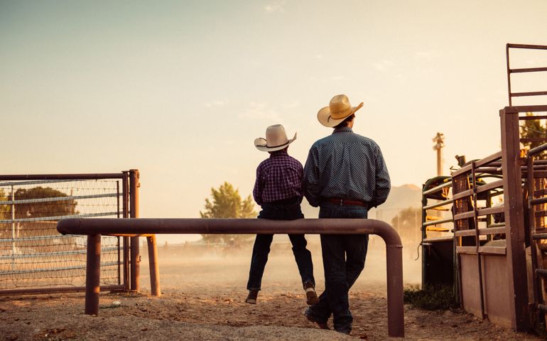 Father and son sitting by rodeo arena at sunrise
