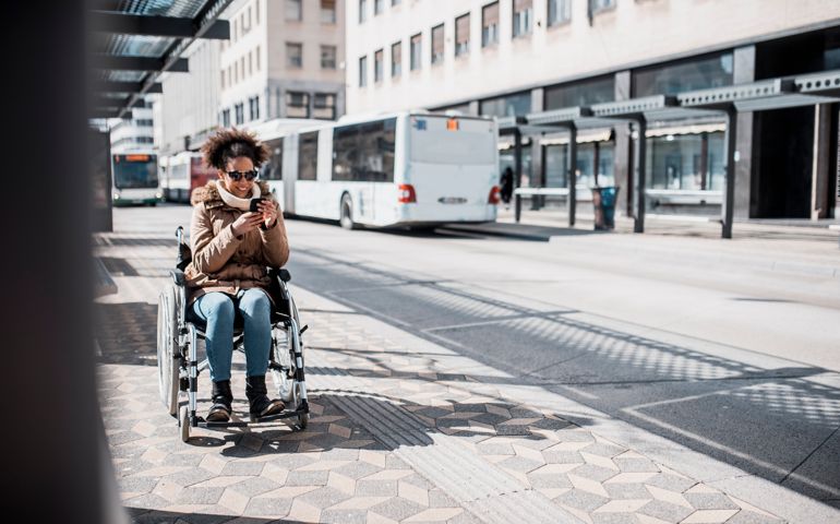 Disabled woman in wheelchair using smart phone and waiting for a bus