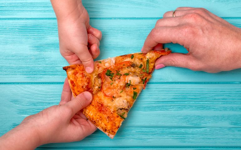 Hands want to take the last piece of pizza from the table.