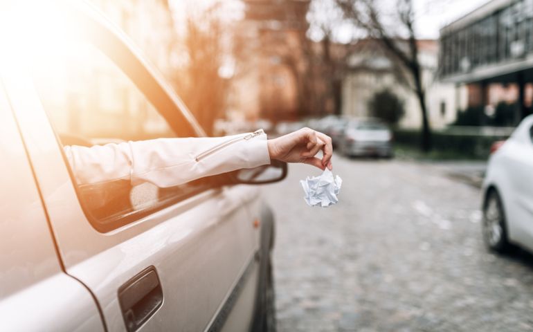 Close-up image of female hand throwing garbage out of car window.