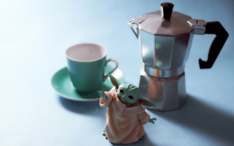Baby Yoda and geyser coffee maker stands on a blue background.