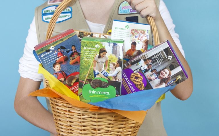 Cadette Girl Scout holding Gift Basket with assortment of ABC Baker's brand Girl Scout cookie boxes.