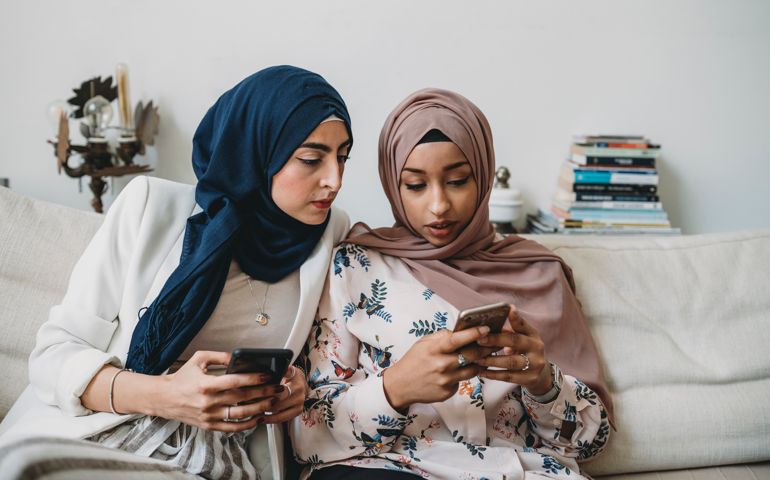 Arab friends using mobile phones sitting on the sofa at home