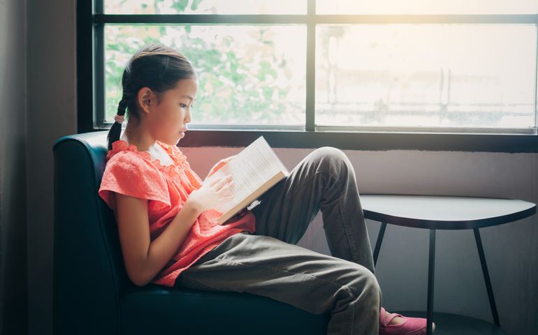 Cute little Asian girl reading a book in the living room at home, Education and knowledge concept