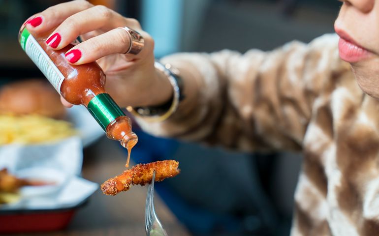 Woman adding hot sauces on crispy, crunchy fried chicken. Fast food