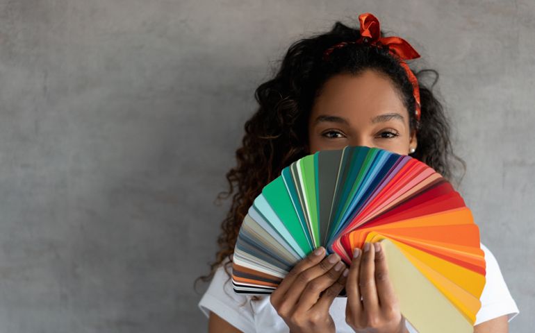 Happy African American woman painting her house and holding a color palette covering her face