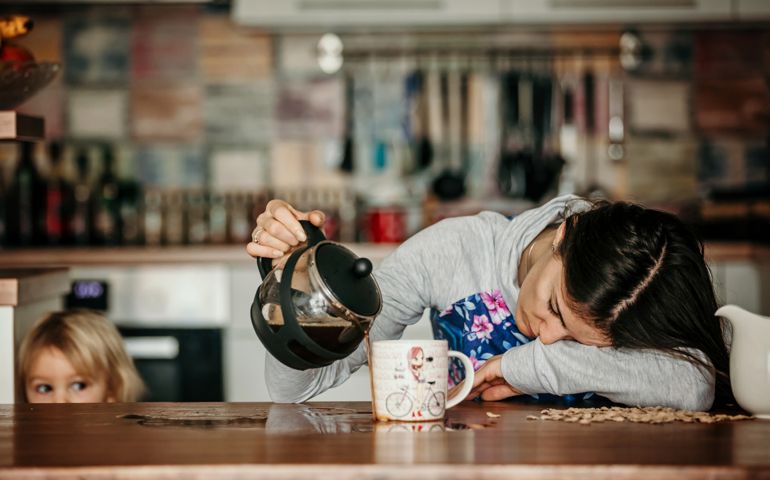 Tired mother, trying to pour coffee in the morning. Woman lying on kitchen table after sleepless night, trying to drink coffee
