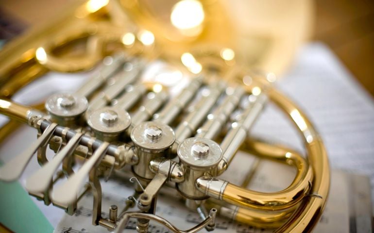 Detail on a French Horn with music sheets on ground.