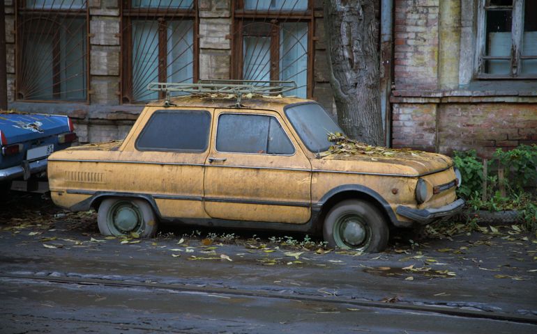 An old, dirty and rusty car parked on the side of a building