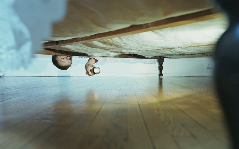 Boy (10-12) looking under bed with flashlight, ground view