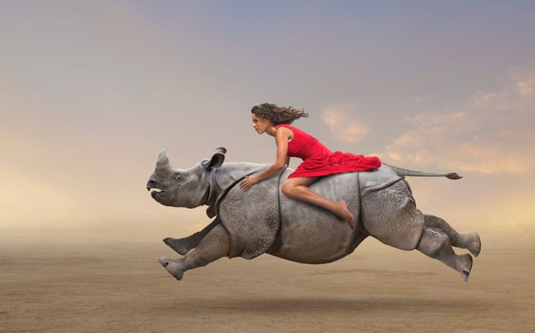 Woman riding rhinoceros in rural field