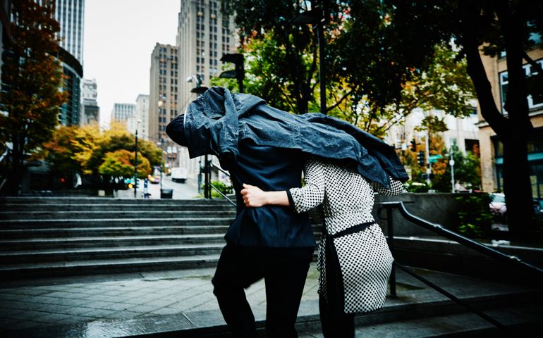 Embracing couple running up stairs in city using coat as shelter from rain