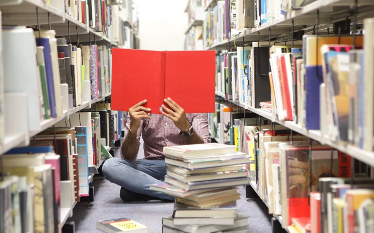 Man sat on floor in library reading red book