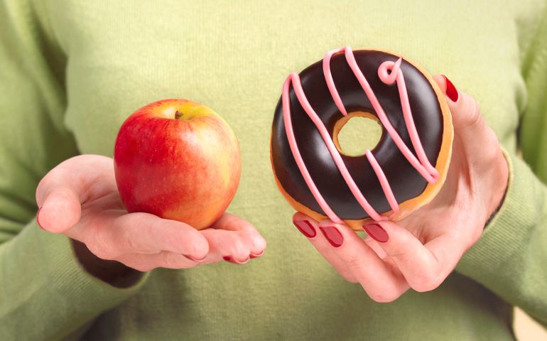 A close up of a woman's hands, one holding an apple the other hand holding a doughnut